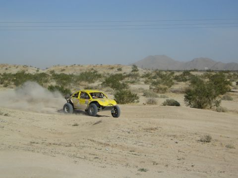Yellow off-road race truck kicking up dust in arid desert terrain