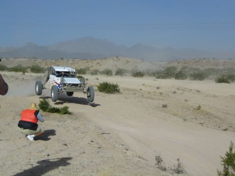 White off-road buggy driving toward a crouching photographer in the desert