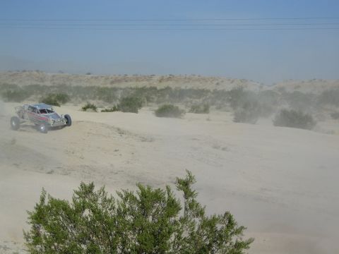 Off-road buggy with headlights on amid heavy dust in the desert