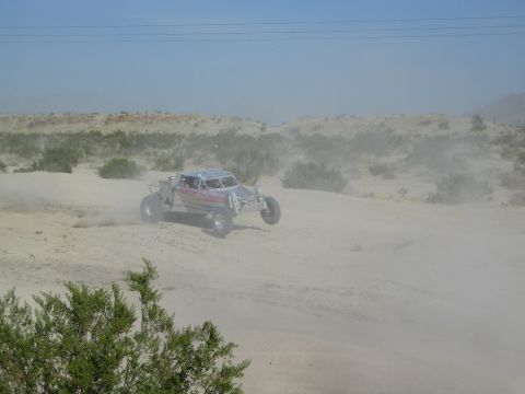 Open-frame off-road buggy racing through dust over sandy desert