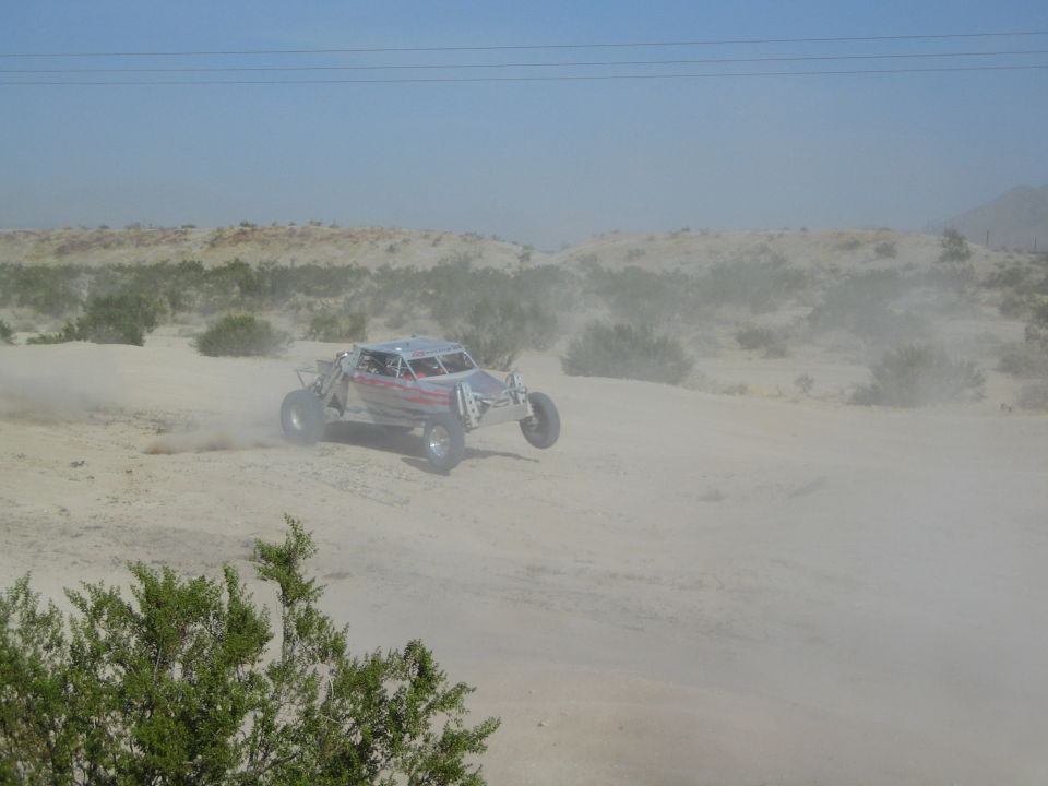 Open-frame off-road buggy racing through dust over sandy desert