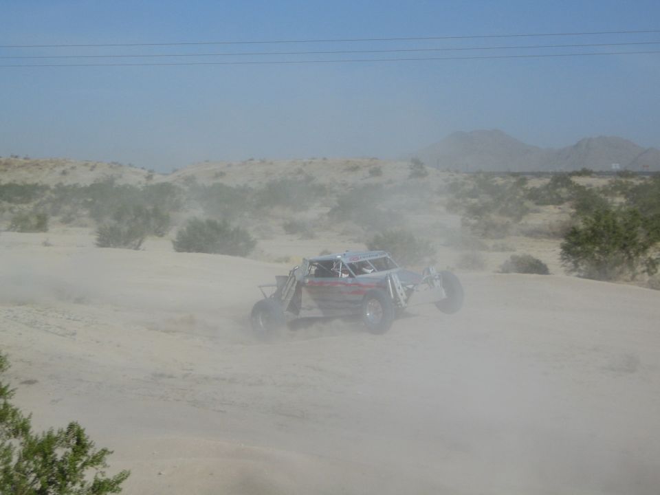 Silver tube-frame off-road buggy turning through heavy desert dust