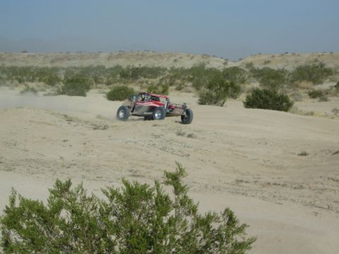 Red and silver off-road buggy cresting a sand rise in the desert