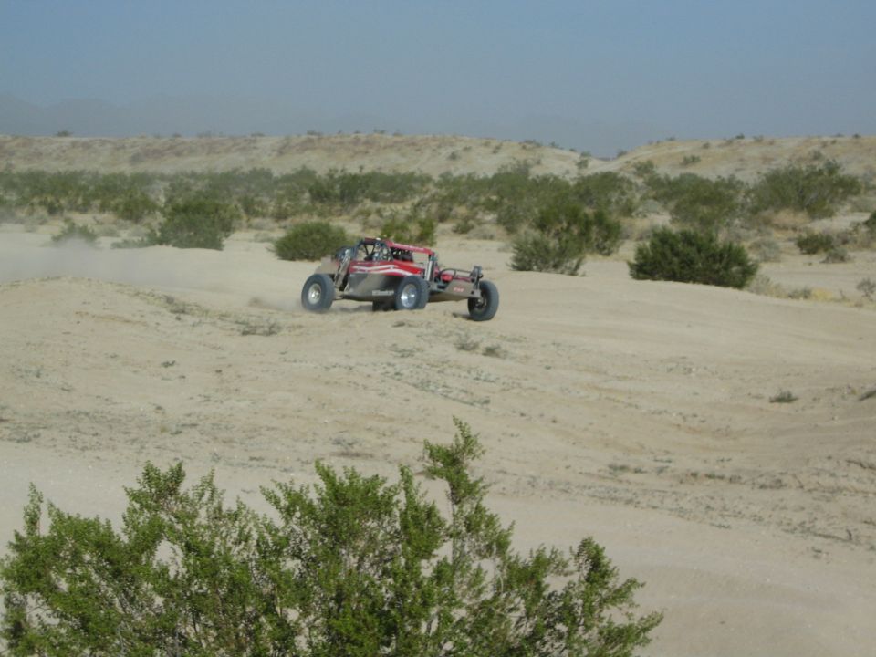 Red and silver off-road buggy cresting a sand rise in the desert