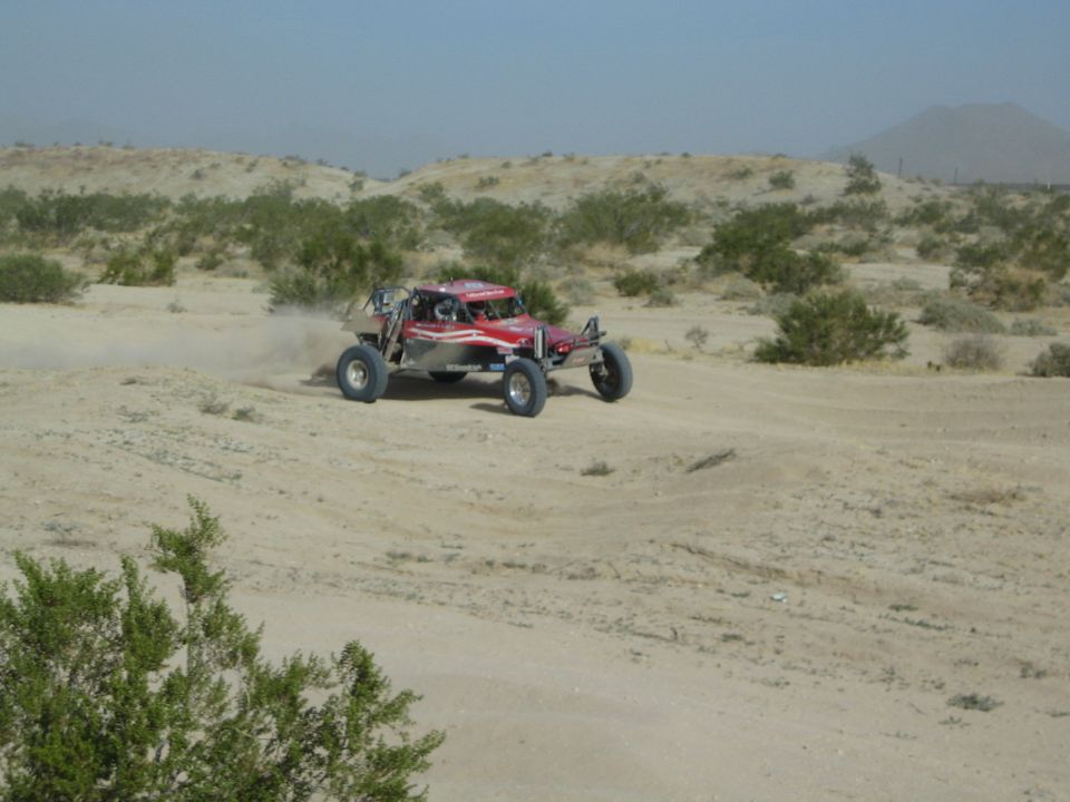 Red off-road race buggy speeding along a sandy desert trail