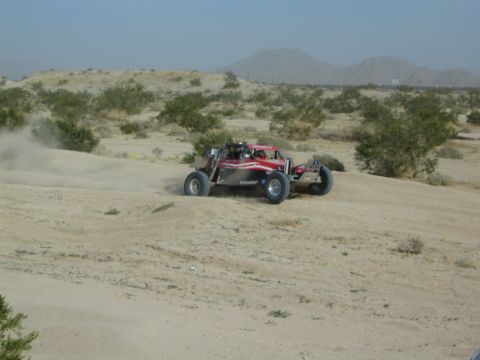 Red and silver off-road buggy turning hard on sandy desert terrain
