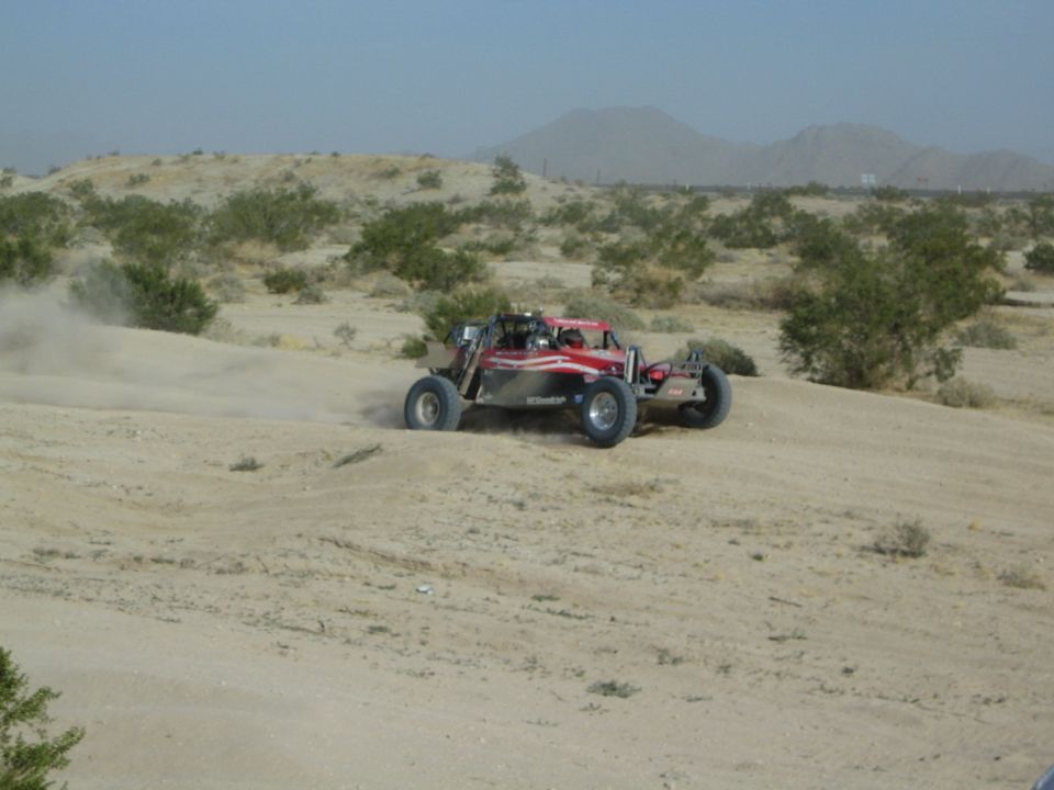 Red and silver off-road buggy turning hard on sandy desert terrain