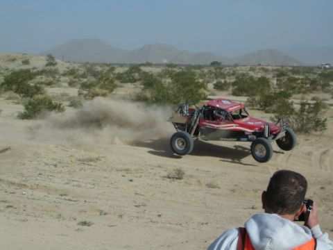 Spectator photographs a red off-road buggy racing through desert dust