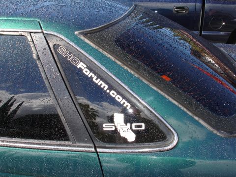 1993 Ford Taurus - A green sedan is parked next to a dark-colored truck, both covered in water droplets.