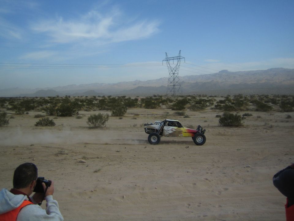 Off-road buggy racing beneath power lines in flat desert scrubland