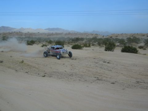 Silver off-road buggy racing across sandy desert with mountains behind