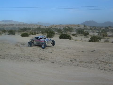Silver off-road buggy cresting a sand dune in open desert