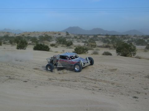 Silver off-road buggy with red flame graphics racing on desert sand