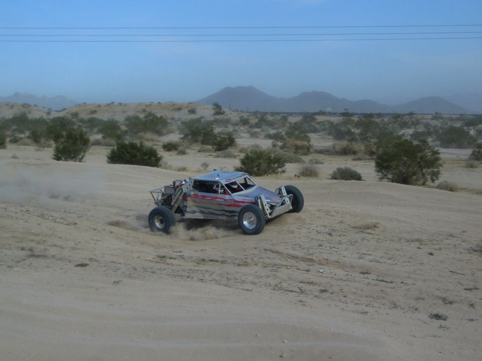 Silver off-road buggy with red flame graphics racing on desert sand