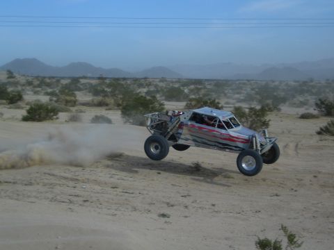 Silver off-road buggy catching air over a sand jump in the desert