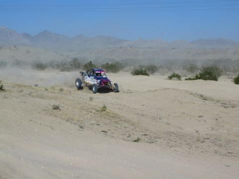 Blue and pink off-road race buggy speeding across sandy desert terrain