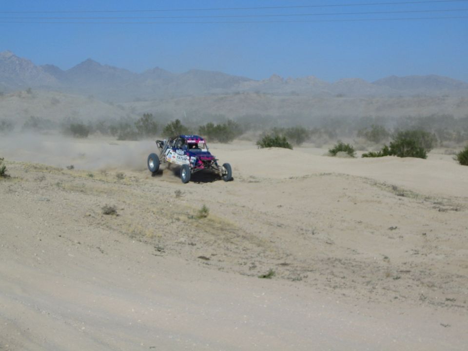 Blue and pink off-road race buggy speeding across sandy desert terrain