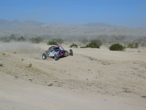 Pink and white off-road buggy racing through desert dust