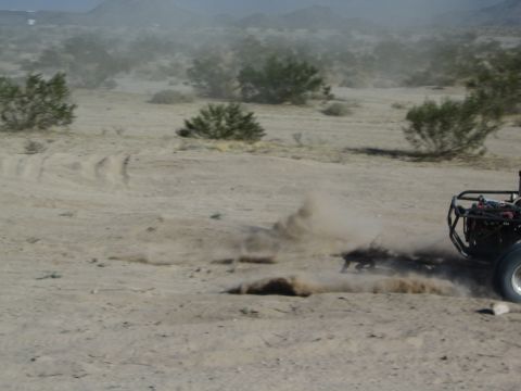 Rear of an off-road buggy spraying dust on a desert track