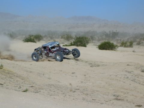 Maroon Alpine-decaled race buggy sliding through desert dust