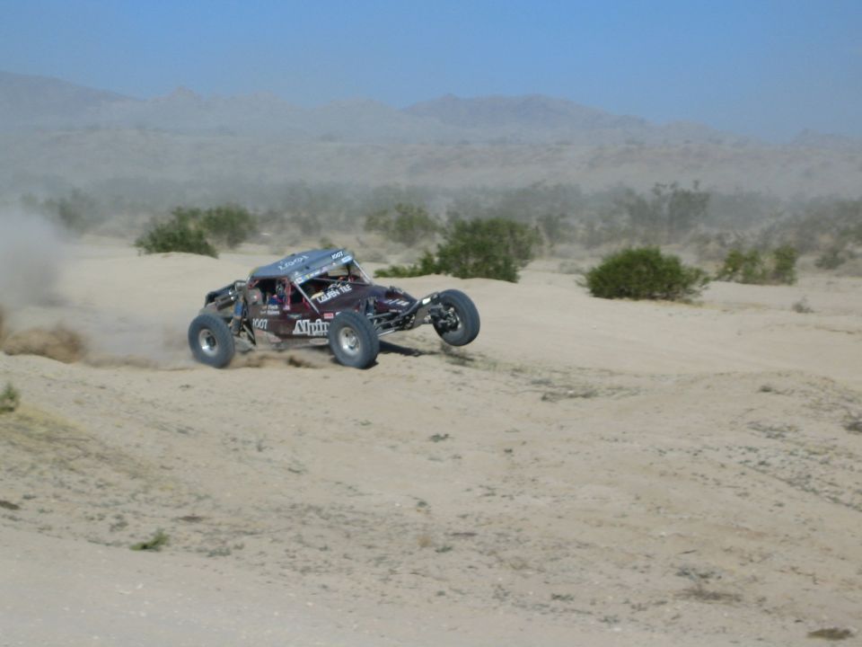 Maroon Alpine-decaled race buggy sliding through desert dust