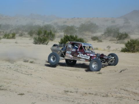 Maroon Alpine number 1007 race buggy speeding in the desert