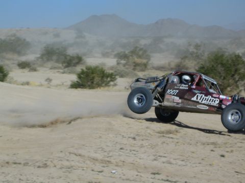 Maroon Alpine 1007 buggy catching air over a desert jump