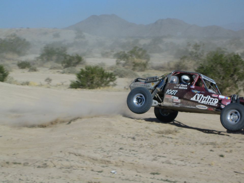 Maroon Alpine 1007 buggy catching air over a desert jump