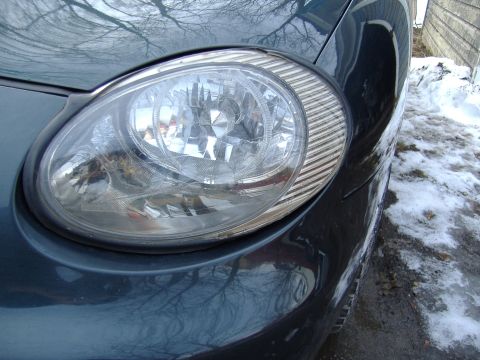 1998 Ford Taurus - Close-up of a 1998 Ford Taurus headlight assembly with snow visible in the background.