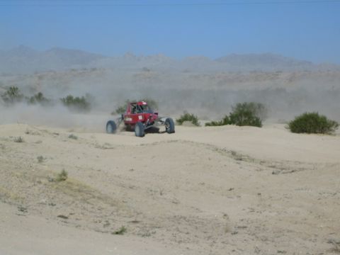 Red off-road race buggy cresting a desert dune
