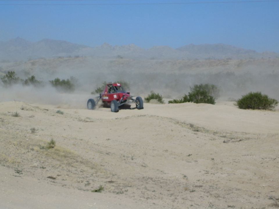 Red off-road race buggy cresting a desert dune