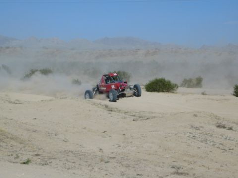 Red off-road race buggy throwing dust on a desert rise