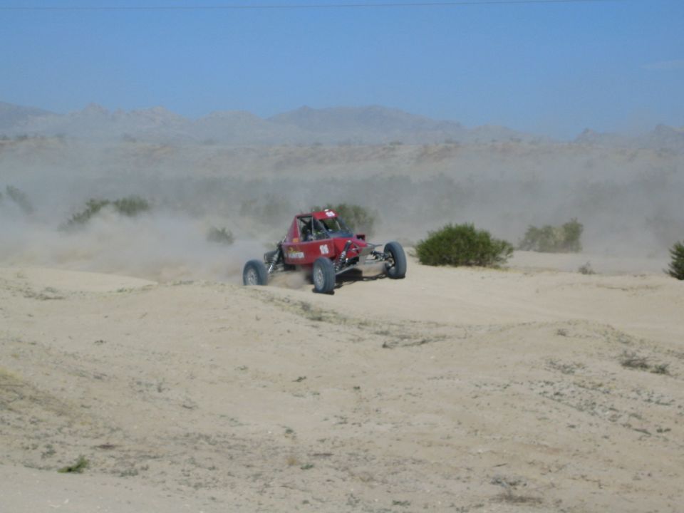 Red off-road race buggy throwing dust on a desert rise