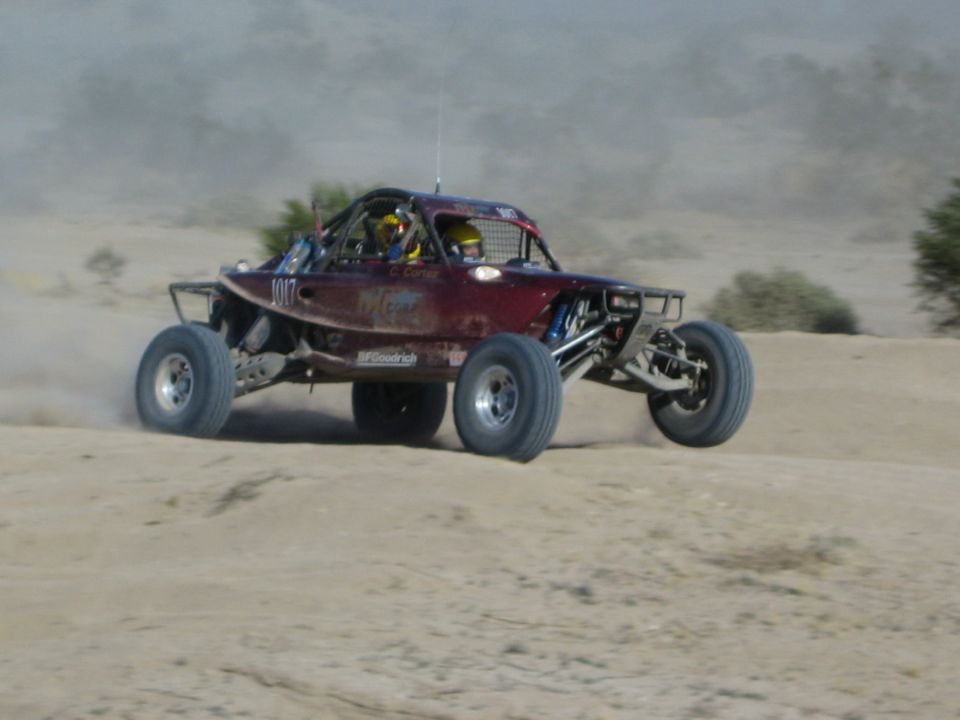Maroon number 1011 race buggy catching air in the desert