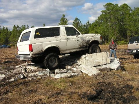 1989 Ford Bronco - A white Ford Bronco navigates an obstacle course of concrete blocks, with a person observing.