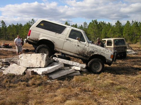 1989 Ford Bronco - A white 1989 Ford Bronco maneuvers over concrete debris during an off-road excursion.