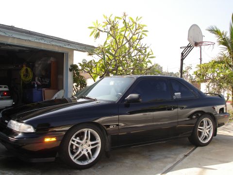 1989 Mazda MX-6 - A black 1989 Mazda MX-6 GT is parked in front of a garage with a basketball hoop in the background.