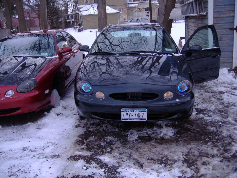 1998 Ford Taurus sedans parked in snow, one dark blue with doors open, one red with black hood