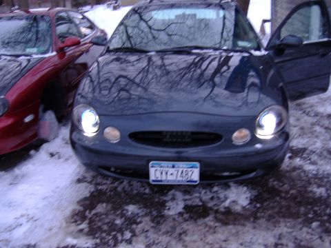1998 Ford Taurus - A dark blue 1998 Ford Taurus is parked in the snow with its driver's door open, next to a red car.