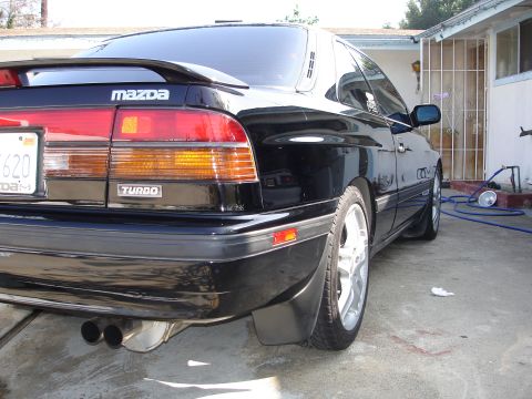 1989 Mazda MX-6 - Rear view of a black Mazda with a spoiler and 'Turbo' badging, parked in a driveway.