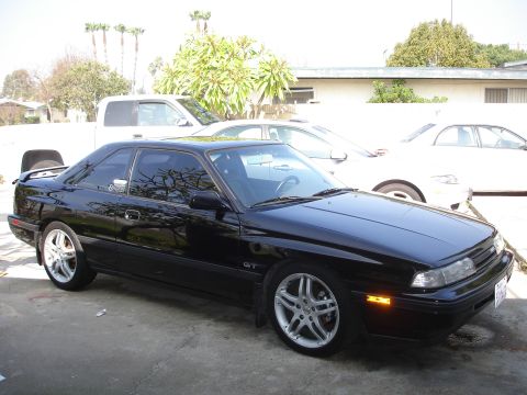 1989 Mazda MX-6 - A black 1989 Mazda MX-6 GT coupe is parked outside with other vehicles in the background.