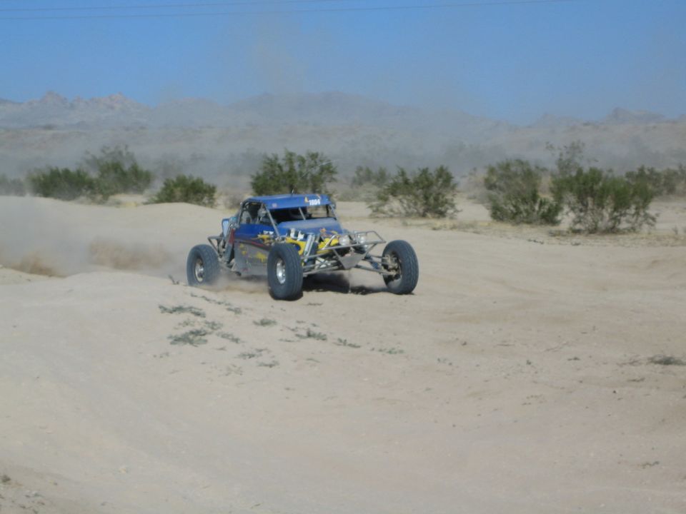 Blue single-seat off-road race buggy throwing dust on a desert sand course