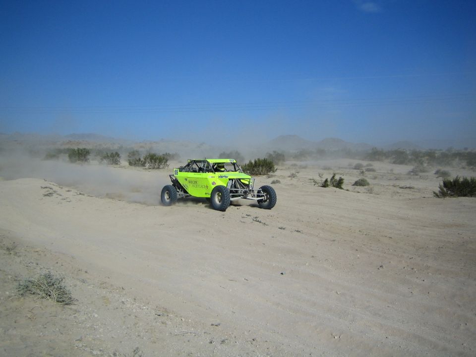 Lime-green off-road race buggy on a sandy desert trail under blue sky
