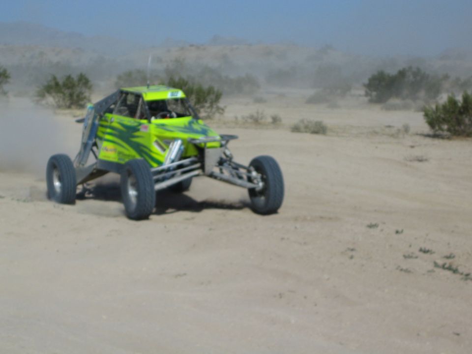 Lime-green and black off-road race buggy racing through desert dust
