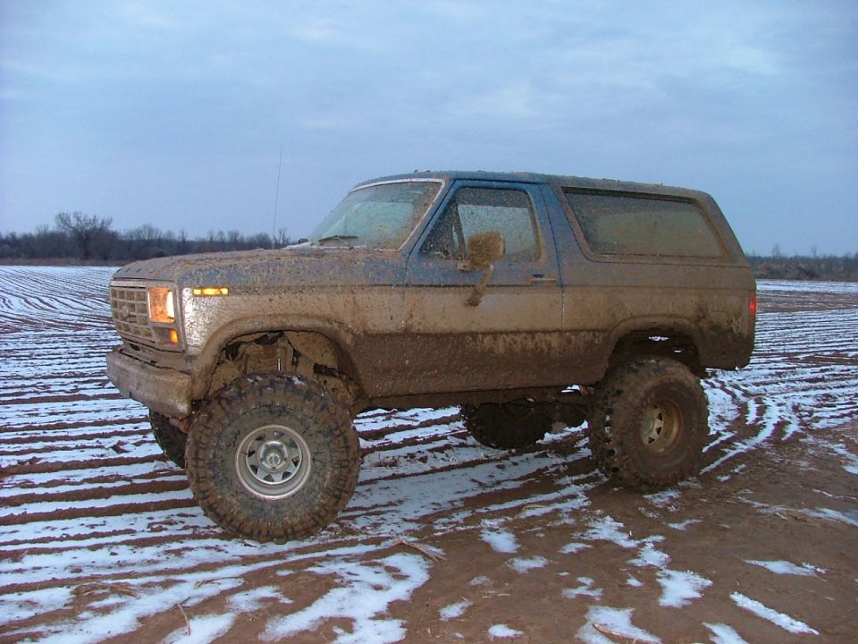 Muddy blue SUV with large tires parked in a field with snow patches