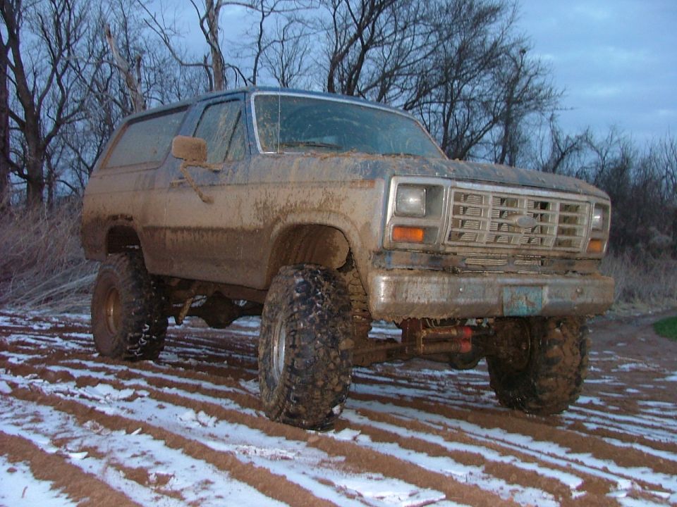 Mud-covered lifted SUV with large tires in a snowy field