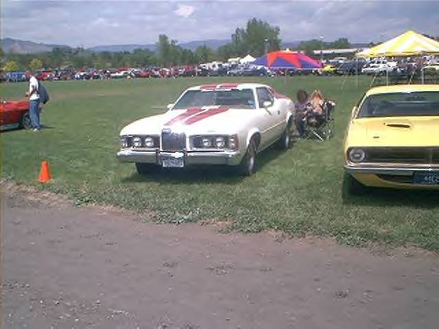 1972 Ford Ranchero with red stripes on hood and roof, parked on grass next to a yellow car