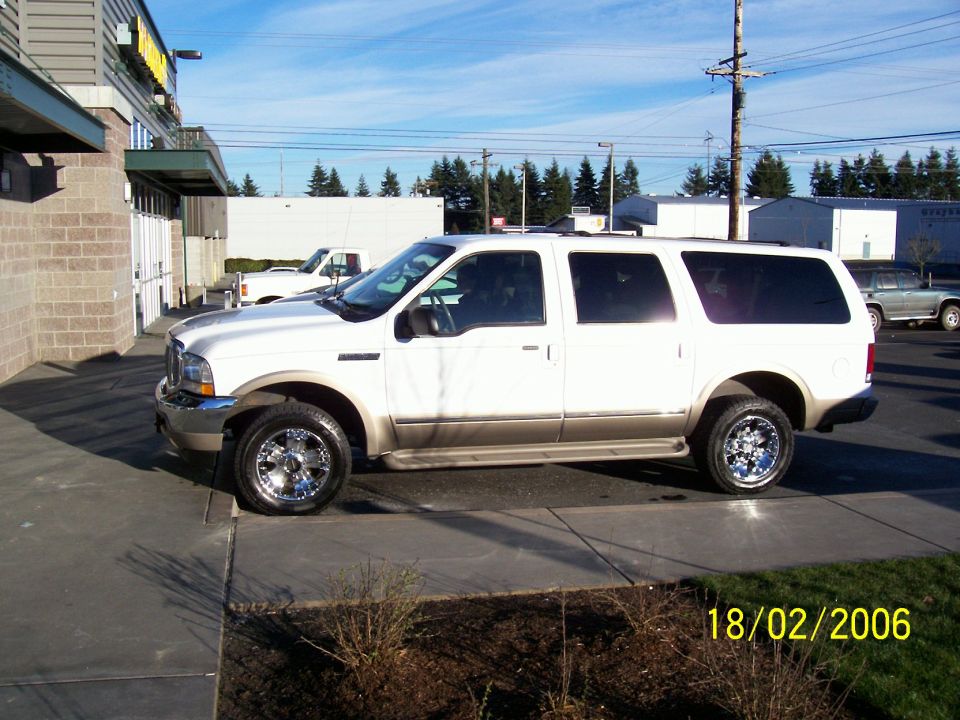 White Ford Excursion SUV with tan lower trim and chrome wheels, side view in a parking lot