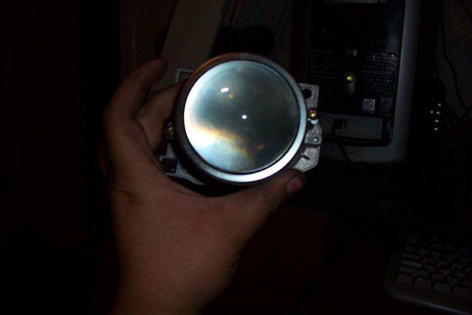 Hand holding a round headlight projector lens, showing reflections on the glass