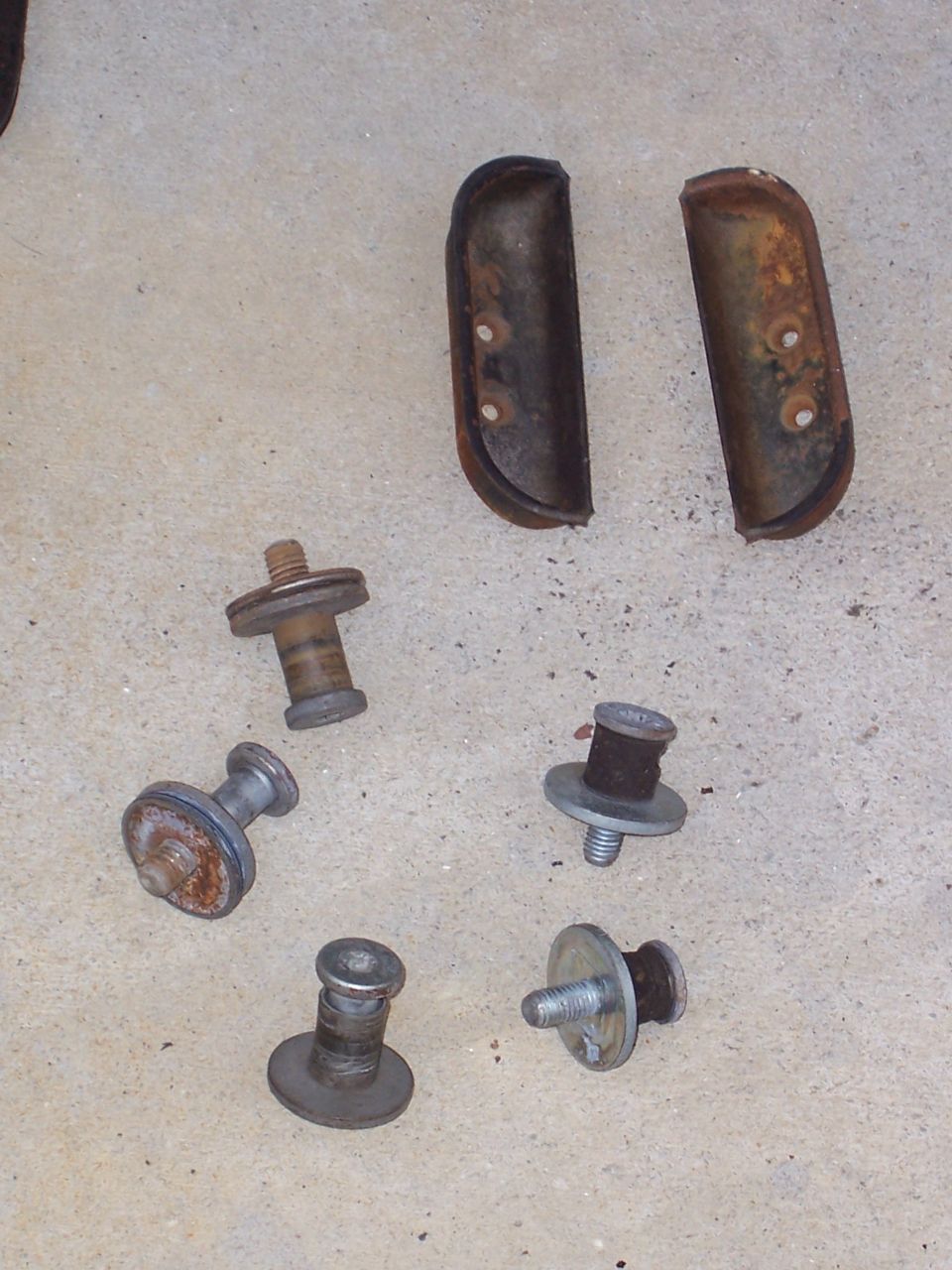 Collection of rusty metal bolts and rubber bumper pieces on a concrete surface